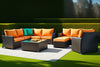 Moderne zwarte wicker loungeset met comfortabele oranje kussens , omringd door groen in de lentezon
